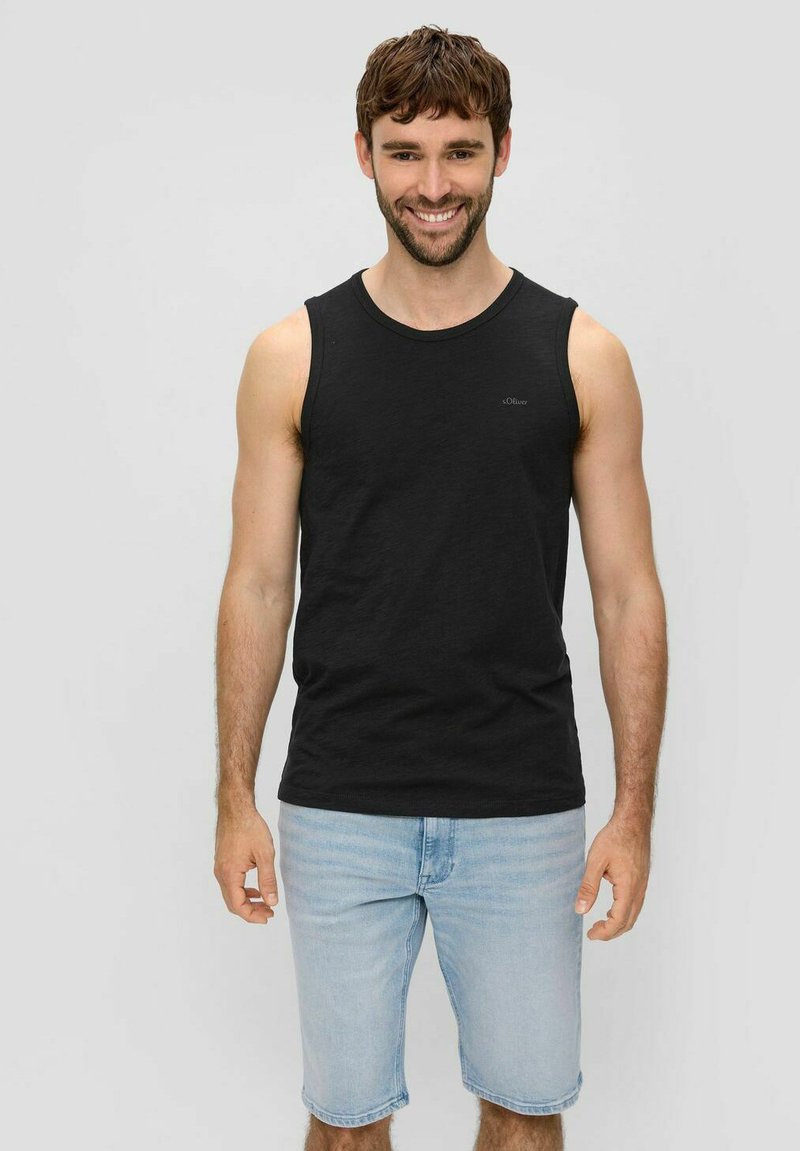 Schwarzes ärmelloses Tanktop aus Baumwolle mit Rundhalsausschnitt und kleinem Logo. Trägt zu hellblauen Jeansshorts.