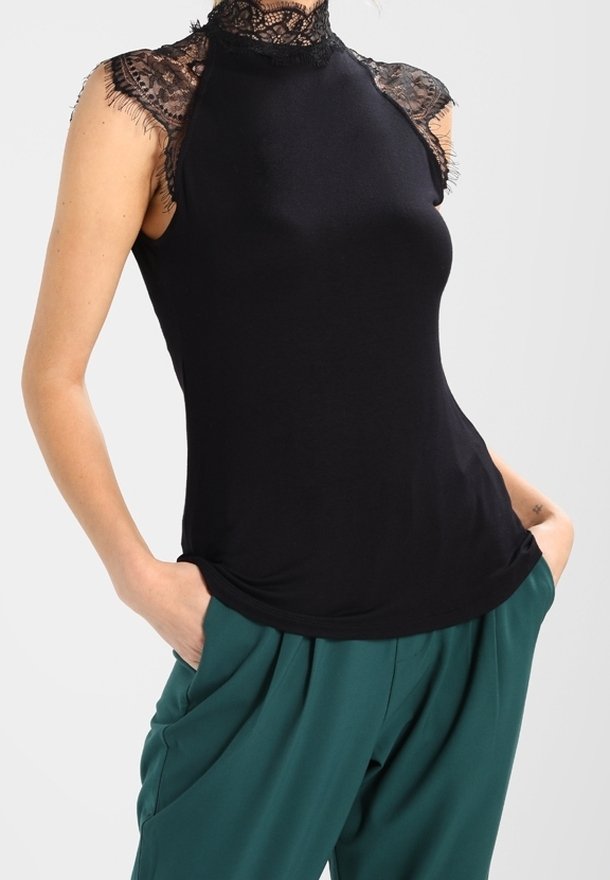 Top negro sin mangas con un alto cuello de encaje y acentos de encaje en los hombros, hecho de un material suave; combinado con pantalones verdes holgados.