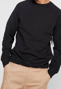 Sudadera negra con pu�ños y cuello de canalé, con un detalle de logo blanco a lo largo de las costuras laterales; tejido suave y texturizado.