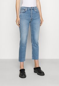 Jeans de tiro medio en azul claro, con pierna recta y dobladillo sin terminar, combinados con zapatos negros de deslizar con forro de piel de pelo.
