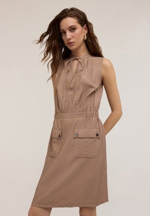 Beige sleeveless dress with a gathered neckline, elastic waist, and two front pockets featuring button details. Soft, textured fabric.