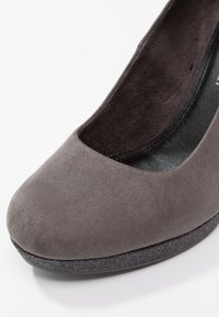 Escarpin fermé en daim gris avec un bout arrondi et une semelle en caoutchouc noir texturé. L'intérieur présente un revêtement lisse noir.