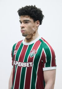 Bordo un zaļš vertikāli svītrots futbols kreklis ar baltiem akcentiem un logotipu uz krūtīm, izgatavots no gludas sintētiskas auduma.