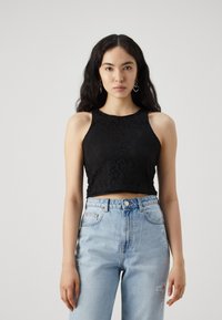 Fekete csipke crop top, kerek nyakkivágással és ujjatlan kialakítással. Világoskék, magas derekú farmernadrággal párosítva, amely kopott részletekkel rendelkezik.