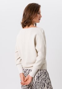 Lichtcrème trui met textuur ribbeling, relaxte pasvorm en brede bootnek. Gelijkend met zwart-wit gestreepte zebrapantalons.