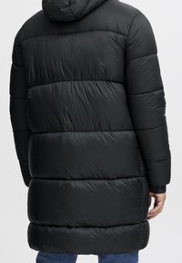 Zwarte pufferjack met capuchon, met doorgestikte secties, elastische manchetten en een knielange snit. Gladde, glanzende textuur.