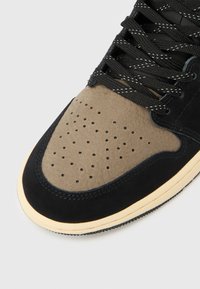 Sapatilha preta e taupe com materiais em camurça e couro, biqueira perfurada, atacadores pretos e entressola bege com sola em borracha.