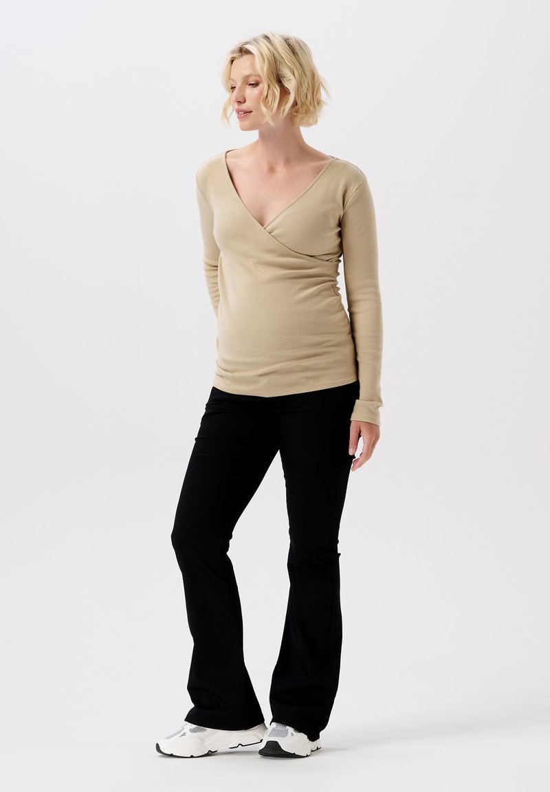 Beige lange mouw top met een V-hals ontwerp, gecombineerd met zwarte flare broeken. De outfit heeft een zachte textuur en een getailleerde silhouette.