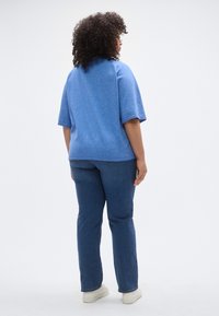 Μπλε πλεκτό τοπ με κοντά μανίκια και υφή, σε συνδυασμό με ίσια σκουρομπλε τζιν και λευκά αθλητικά παπούτσια, φωτογραφία από πίσω.