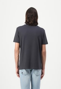 Grå bomulls T-skjorte med korte ermer og rund hals, vist fra baksiden. Kombinert med lyseblå denimjeans.