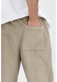 Beige fløjlsbukser med synlig sidelomme, lige snit og tekstureret ribstruktur. Bruges med en løstsiddende hvid skjorte.