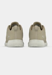 Bej sportcipők textúrázott szövetfelsővel, kerek sarokkal és fehér gumitalppal. Jellemző rá a minimális márkázás az oldalon.