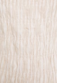 Tessuto beige chiaro con strisce orizzontali bianche, caratterizzato da arricciature testurizzate e dettagli raccolti, creando un motivo ondulato.
