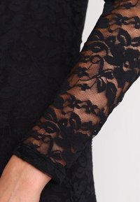 Czarna koronkowa rękaw o kwiatowym wzorze, przezroczysta siateczkowa faktura oraz solidny czarny mankiet. Projekt prezentuje misternie wykonane detale i warstwy tkaniny.