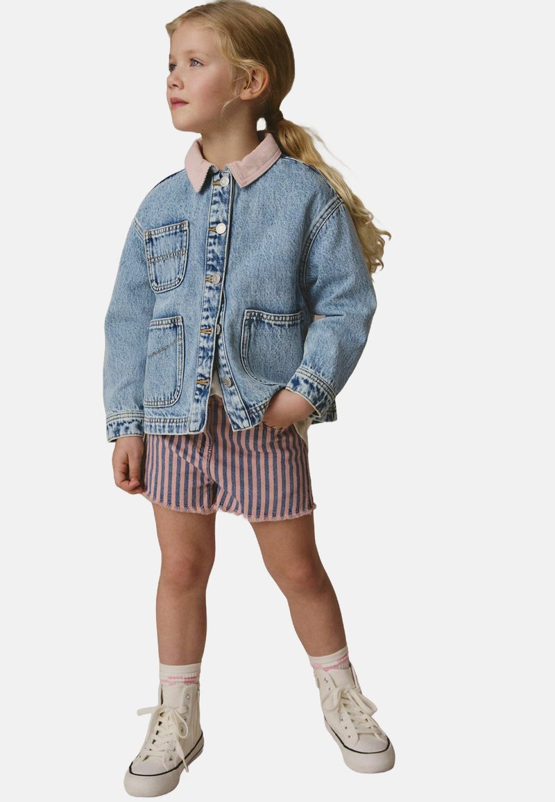 Chaqueta de mezclilla con lavado azul claro y cuello rosa, combinada con pantalones cortos a rayas rosas y azules. Zapatillas altas blancas completan el look.