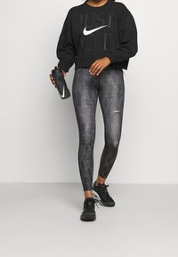 Sweat-shirt noir court avec texte "JUST DO IT" et logo Nike blanc, associé à un legging noir avec un motif répétitif blanc Nike.