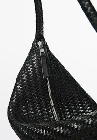 Sac hobo en cuir tressé noir avec une fermeture éclair en métal argenté et une bandoulière tressée, posé sur un fond blanc.