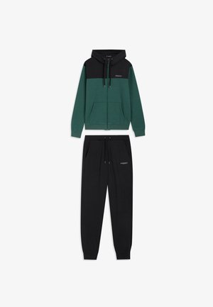 Sudadera con capucha de cremallera en verde y negro con bolsillos tipo canguro, combinada con pantalones de chándal negros con cintura elástica y detalle de logo.