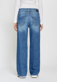 Wide-leg blue jeans in faded denim, featuring two back pockets and seam detailing along the waistband. Flat hem with slight fraying.