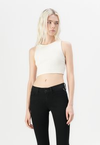 Kremasti rebrasti crop top s okruglim izrezom, uparen s crnim uskim trapericama koje imaju prednje dugme i bočne džepove.