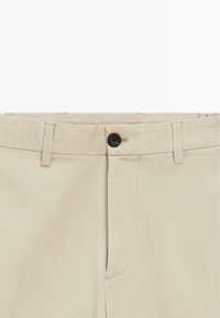Beige pants featuring a black button, flat front with subtle stitching details, and side pockets. Made from cotton-blend fabric, smooth texture.