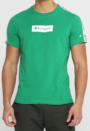 Camiseta verde de manga corta hecha de algodón. Presenta un parche de logo blanco en el pecho y detalles en negro con estampado en las mangas.