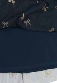Top de color azul marino con una tela suave y una superposición de malla que presenta pequeños patrones de lazo dorado. Los materiales combinan texturas y colores de manera fluida.