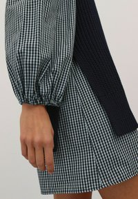 Kleid mit einem schwarz-weißen Vichy-Muster, ausgestattet mit einem strukturierten marineblauen Strickdetail an der Seite und Puffärmeln.