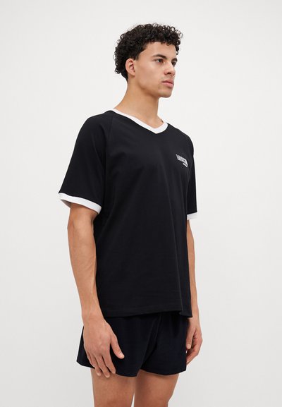 T-shirt preto com decote em V e borda branca no decote e nas mangas. Feito de algodão, apresenta um gráfico de marca no peito. Tem um corte descontraído.