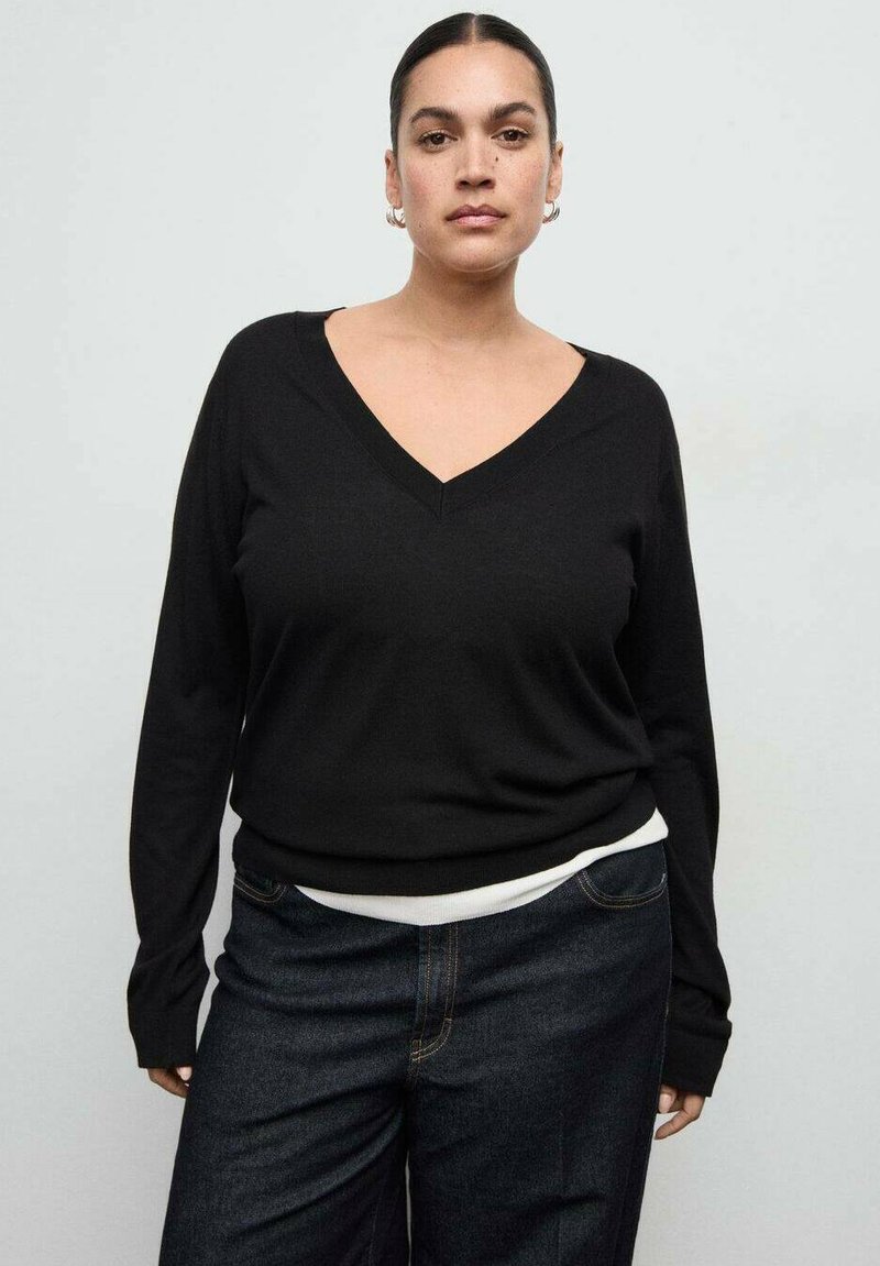 Maglione nero con scollo a V, maniche lunghe e vestibilità comoda, abbinato a jeans in denim scuro con una fascia vita bianca a contrasto.