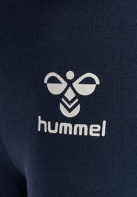 Mørkeblå træningsleggings med et hvidt grafisk logo og teksten "hummel" nær taljen, lavet af et glat, strækbart materiale.