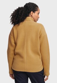 Beige Fleecejacke mit hohem Kragen, lockerer Passform und strukturierter Oberfläche. Verfügt über überschnittene Schultern und eine gerade Rückennaht.