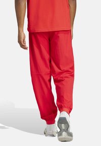 Red athletic pants made from lightweight material, featuring elastic cuffs, side seams, and a relaxed fit. Worn with white sneakers.