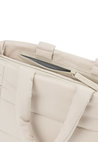 Vaaleanbeige tikattu kantokassi, jossa on kestäviä kahvoja, vetskari ja sileä sisävuori. Varustettu logolla vetoketjun vedin.