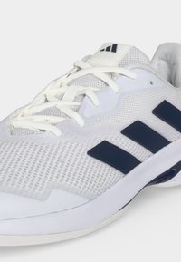 Chaussure de sport en mesh blanc avec des rayures bleu marine, des lacets blancs et un col rembourré sur un fond clair.