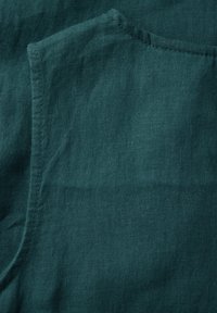 Turkusowa lniana tkanina o miękkiej fakturze, z prostym, nieozdobnym wzorem i widocznym szyciem wzdłuż krawędzi.