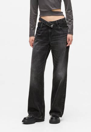 Black high-waisted wide-leg jeans with tonal stitching, an asymmetrical waistband, and a slight faded texture. Worn with black platform shoes.