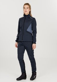 Marinblått träningsset som innehåller en figursydd jacka med färgblockeringsdesign och dragkedjefickor, parat med matchande slim-fit byxor och robusta svarta kängor.