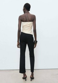 Haut crème sans manches avec un design plissé, associé à un pantalon noir ajusté et des sandales à talons noirs. Les accessoires comprennent des bracelets empilés.