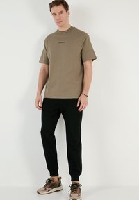Olivengrøn bomulds t-shirt med rund hals og korte ærmer, parret med sorte joggers og multifarvede sneakers med snørebånd og hardware detaljer.