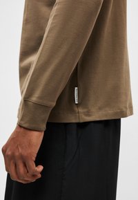 Helepruun pikkade varrukatega särk, millel on sile puuvillane tekstuur. Sellel on küljetähis ja lõdvestunud lõige, sobitub mustade pükstega.