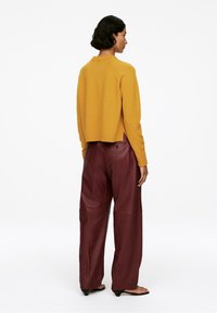Senfgelbes, gekürztes Sweatshirt mit geripptem Halsausschnitt und Saum; kombiniert mit burgunderfarbenen Lederhosen mit Seitentaschen und einer glatten Oberfläche.