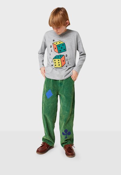 Camisa de manga larga gris con gráfico de dados coloridos; pantalones de pana verde con formas azules. Zapatos marrones. Conjunto informal para niños.