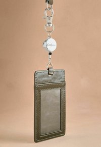 Držák na karty v olivově zelené barvě s texturovaným povrchem, průhledným průkazovým průchodem a kovovým zatahovacím navijákem. Obsahuje stříbrnou sponu pro přichycení.