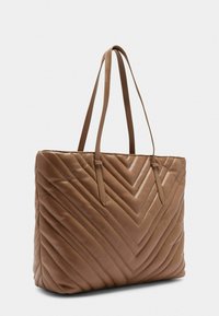 Borsa tote in pelle marrone con motivo a zig zag trapuntato e due manici lunghi. Texture liscia con dettagli di cucitura sui bordi.