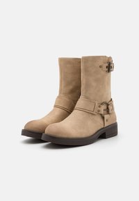 Bottines en daim beige avec bout rond, dotées d'une boucle et d'une sangle sur le côté, ainsi que d'un petit talon carré marron. Texture lisse, design minimaliste.