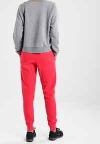 Grå sweatshirt med ribbat avslut och ärmslut, i kombination med ljusrosa joggers med avsmalnande ben och dragsko i midjan. Svarta träningsskor.