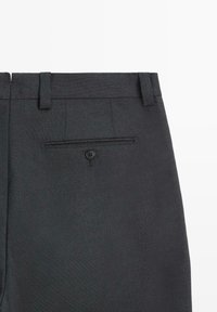 Pantalon gris foncé à surface texturée, avec passants pour ceinture, une poche arrière avec fermeture à bouton, et des détails de coupe ajustée.
