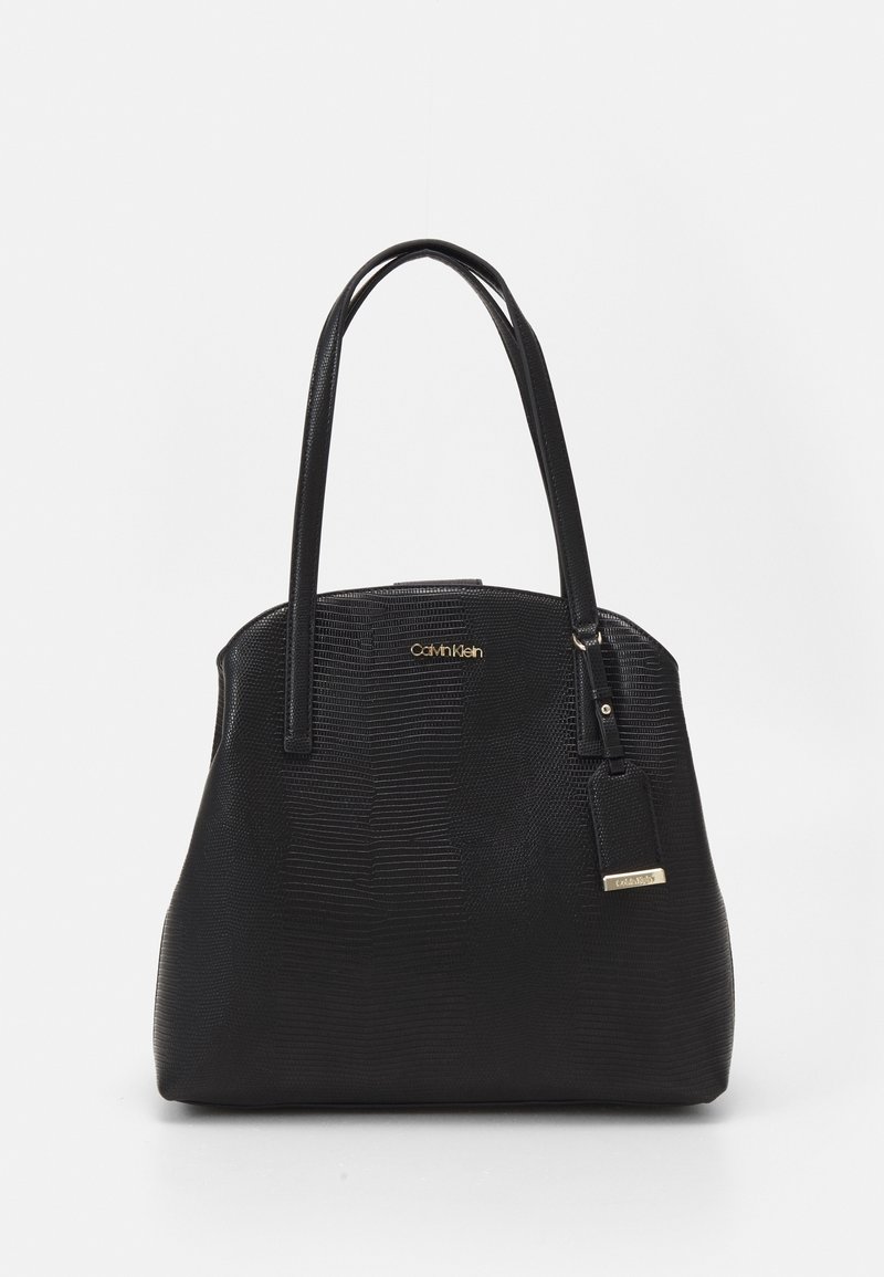 Sort taske med tekstureret yderside, buet form og to håndtag. Har et gyldent logo og en matchende mærkat til detaljer.