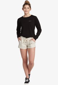 Black long-sleeve shirt with "ROXY" logo, paired with beige linen shorts featuring an elastic waist and drawstring. Black sneakers complete the look.
